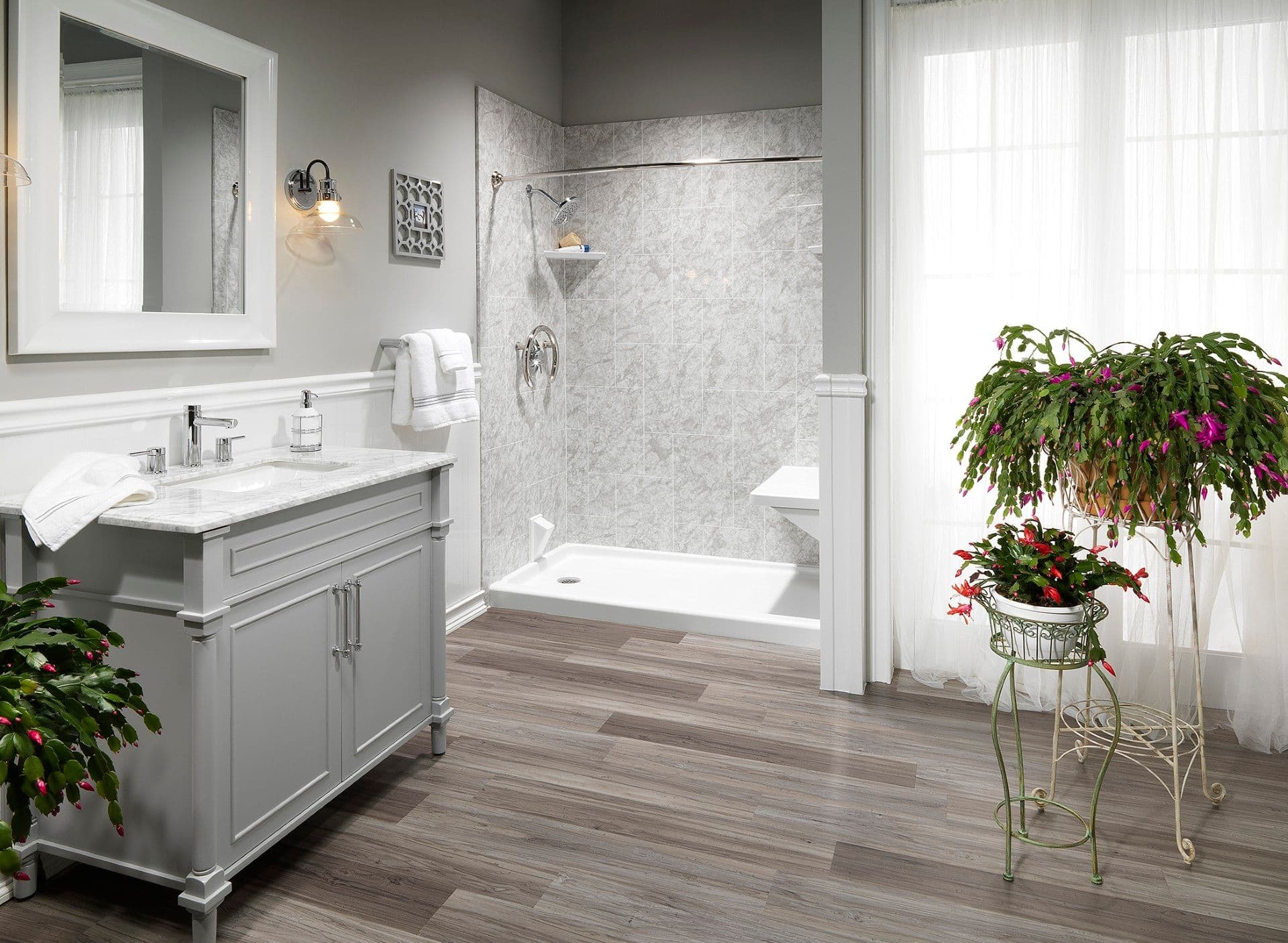 Bright, accessible bathroom featuring a low-threshold walk-in shower with a built-in bench seat, gray marble-look wall surround, white vanity with marble countertop, wood-look flooring, and large windows that fill the space with natural light.