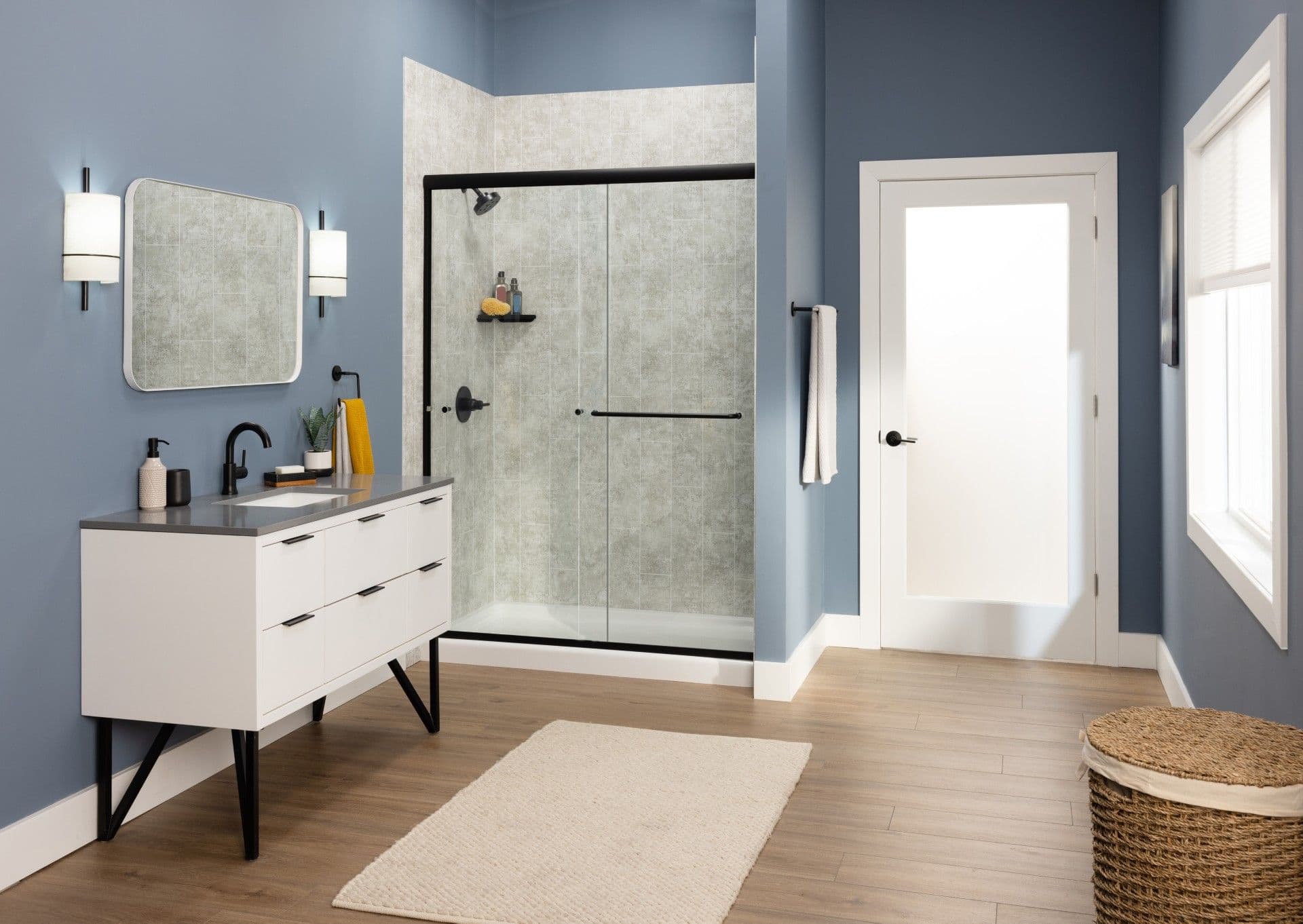 Modern bathroom featuring a spacious walk-in shower with a black-framed sliding glass enclosure, light gray wall surround, blue accent walls, white floating vanity with black fixtures, wood-look flooring, and clean contemporary finishes.